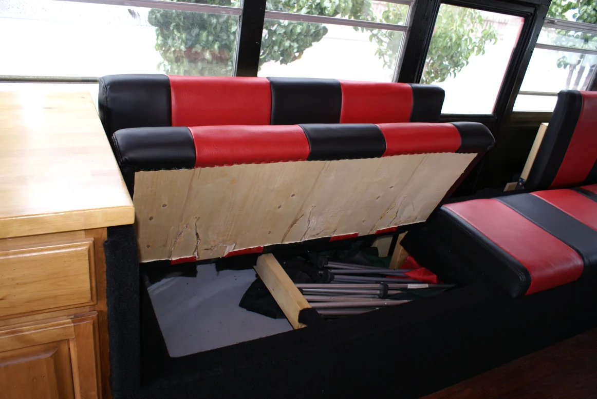 A bench seat lifted open to show storage underneath, packed with folding chairs