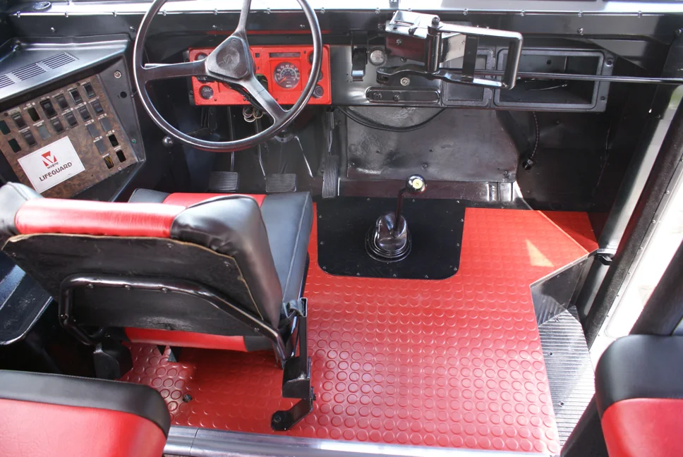 Looking down at the driver area: red rubber floor, black dash and steering wheel