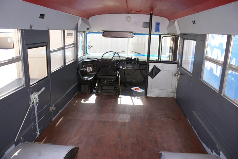 The stripped bus interior with new gray walls, red ceiling and wood-look floor
