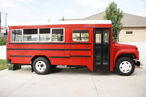 The finished bus in red with black stripes and a white roof, parked in a driveway