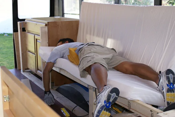 A crew member stretched out testing a newly built bench inside the bus