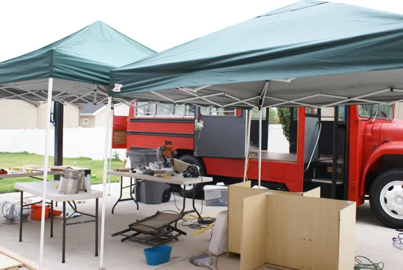 The outdoor workshop: canopies, tools and cabinets beside the red bus