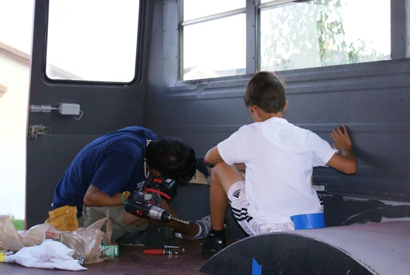 A crew member and a young helper fitting panels inside the bus