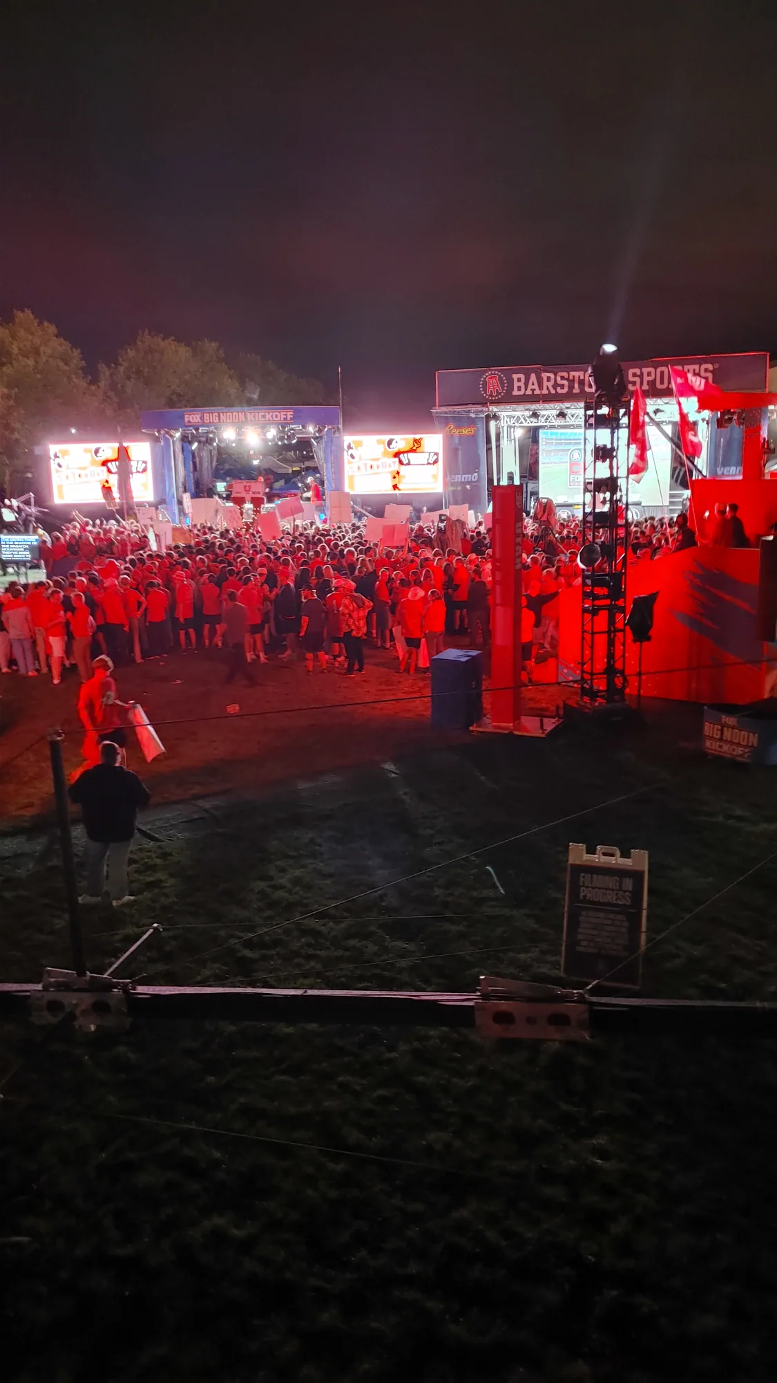 The tailgate lot at night lit red under the stadium lights
