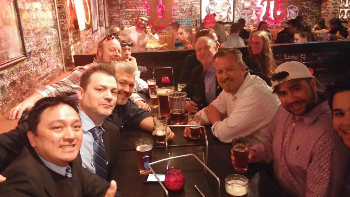 Phi Delt brothers crowded around a table at a bar, raising drinks
