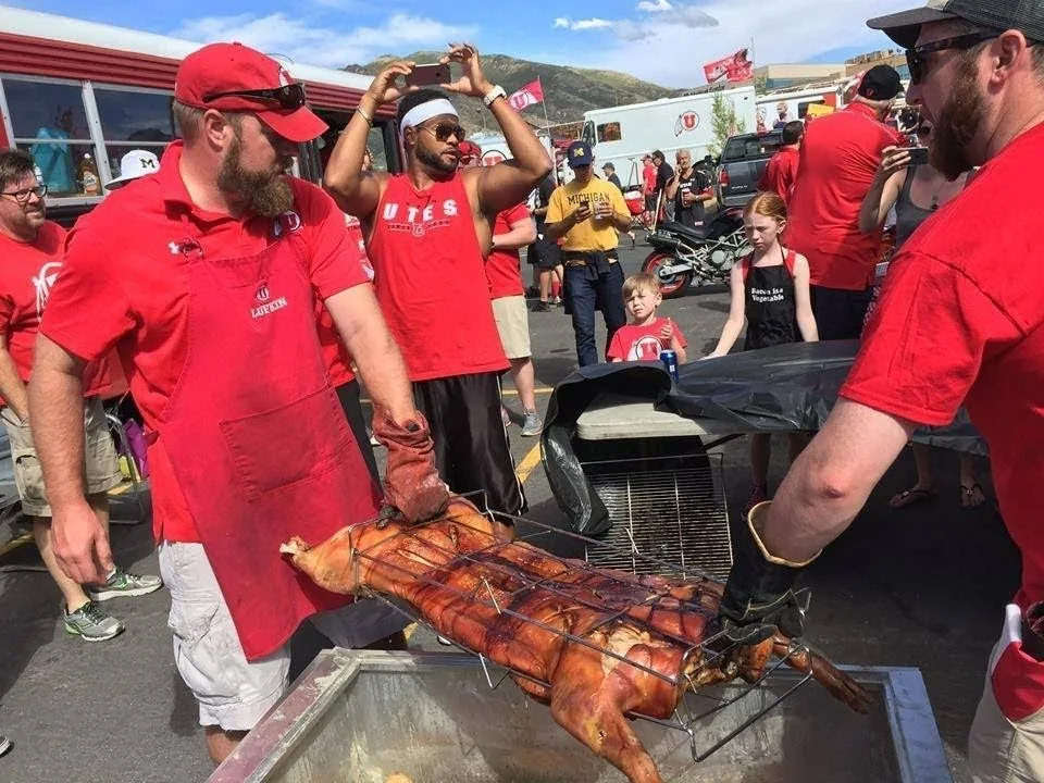 Crew in red shirts working a whole pig on a large outdoor roaster at the tailgate