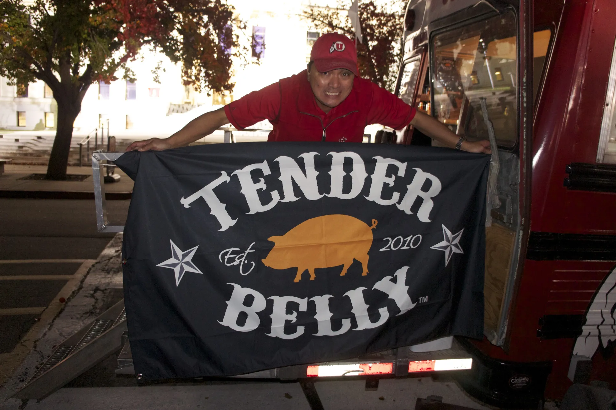 A crew member holding up a black Tender Belly flag beside the bus