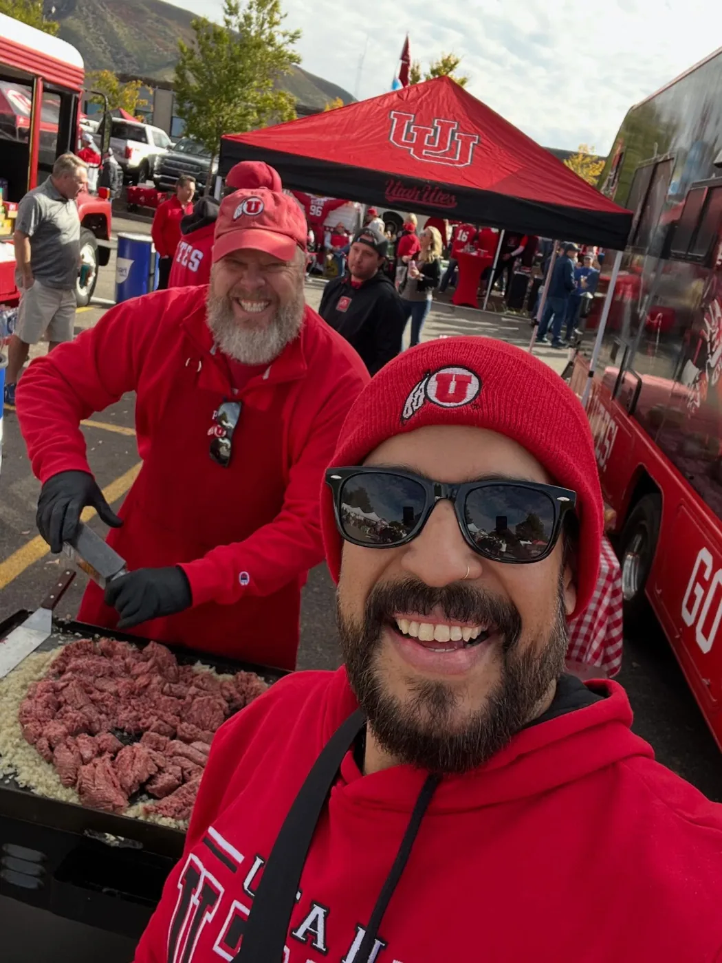 Two crew members grinning beside a flat-top full of steak and onions