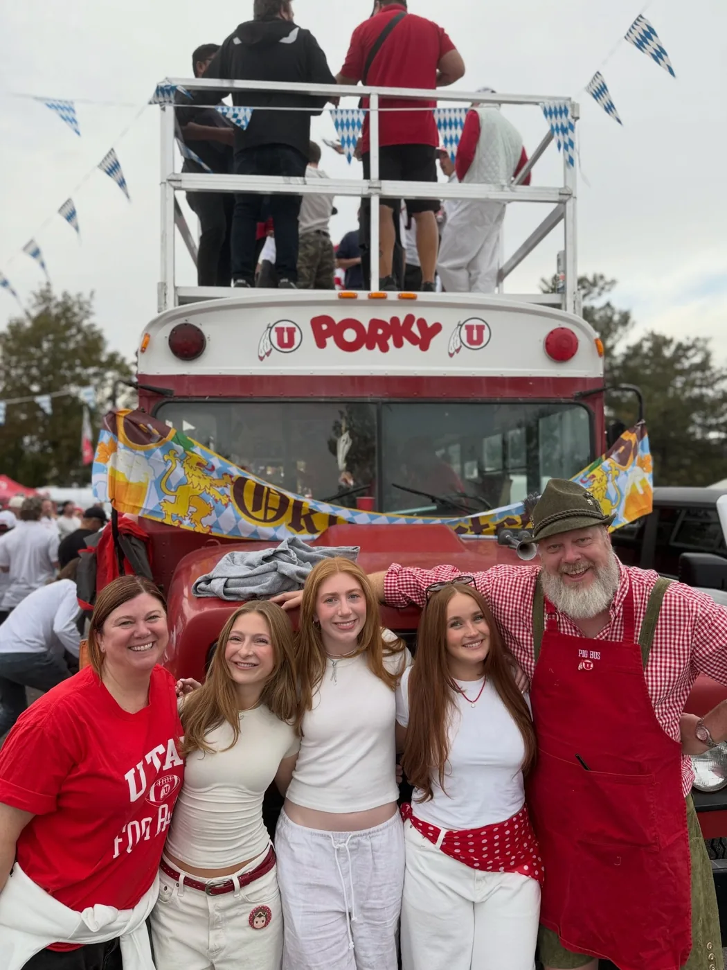 Friends and a crew member in an Alpine hat and red apron in front of Porky’s Oktoberfest banner