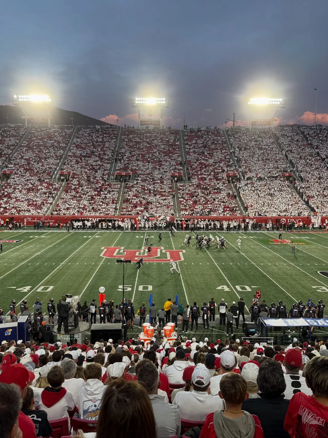 Rice-Eccles Stadium under the lights, packed in red and white, viewed from the stands