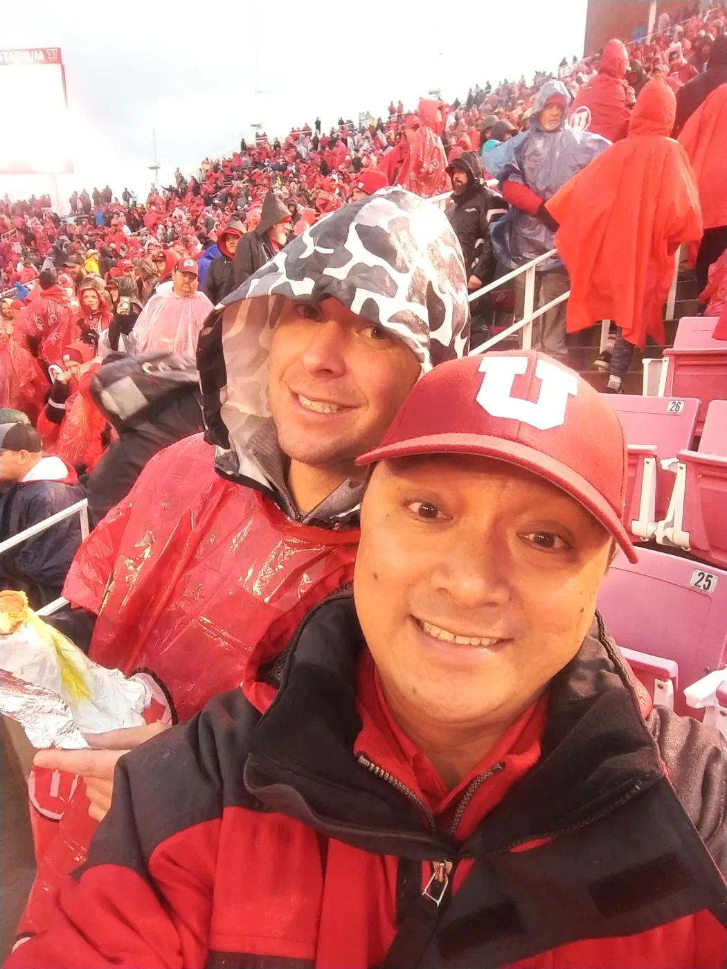 Two crew members in rain gear taking a selfie in the stands at a rainy game