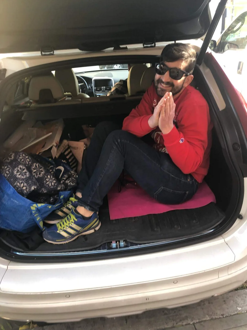 A friend in a red sweatshirt riding in the back of an SUV, hands together