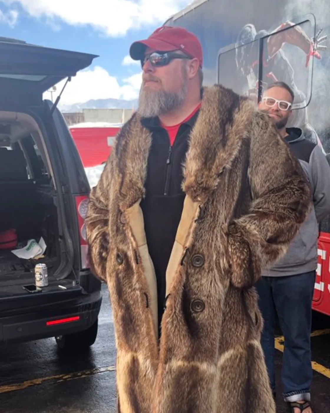 A crew member in a full-length fur coat and Utah cap beside a tailgate SUV