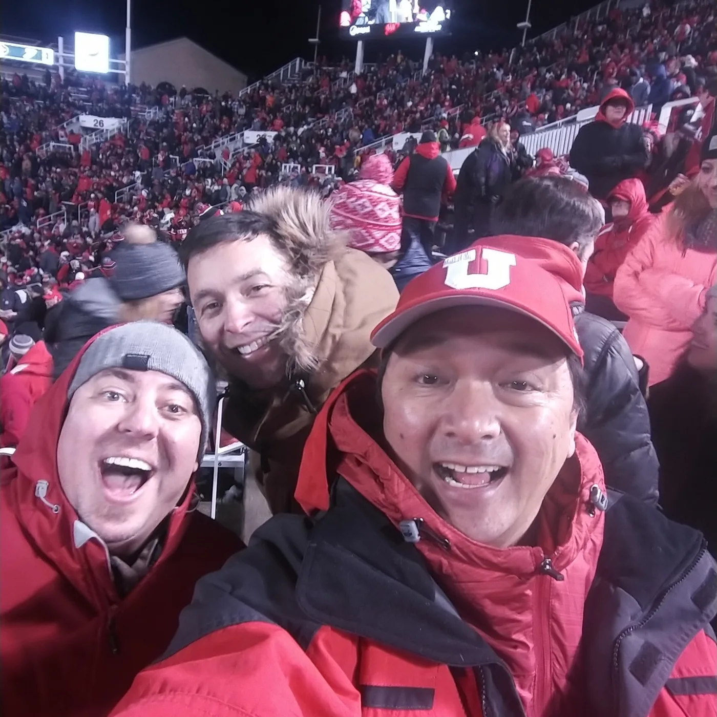Three friends in winter coats grinning in a night selfie at Rice-Eccles